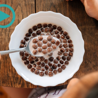 Photograph of a child at a wooden table with chocolate cereal on a spoon, taken from above 