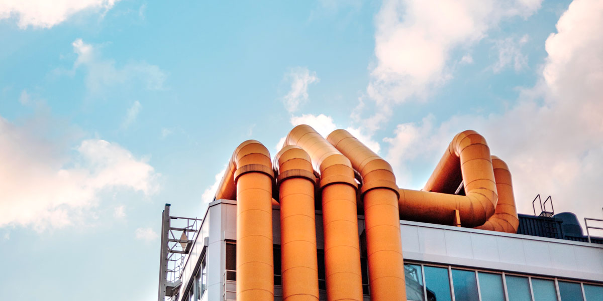 Industrial architecture with orange pipe structure against a cloudy blue sky.